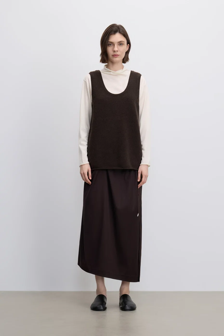 Brown sleeveless top layered over ivory sleeves with a tonal midi skirt.