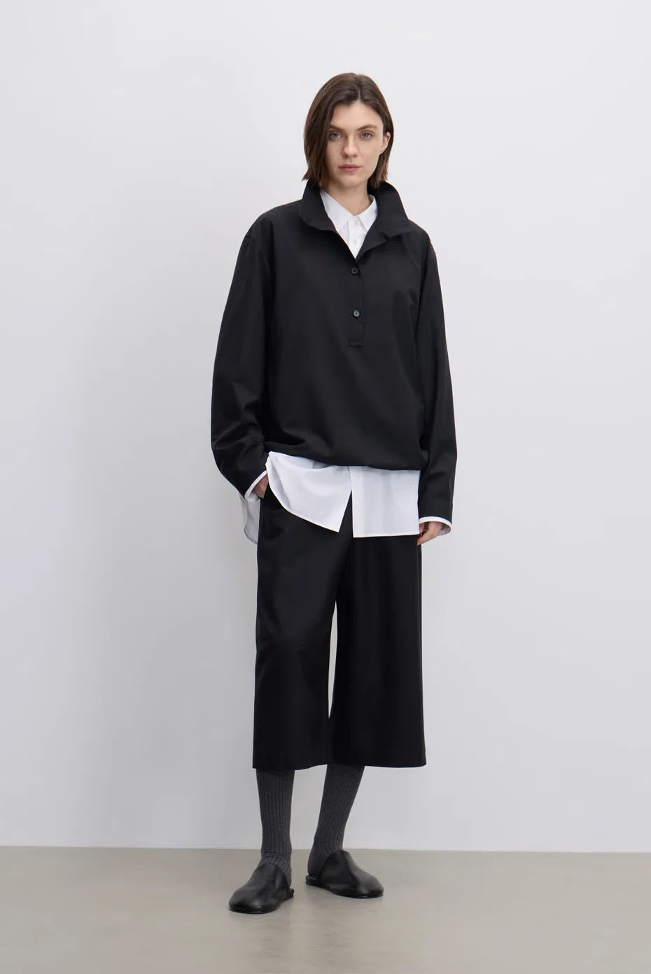 Black jacket layered over a long white shirt with black culottes.