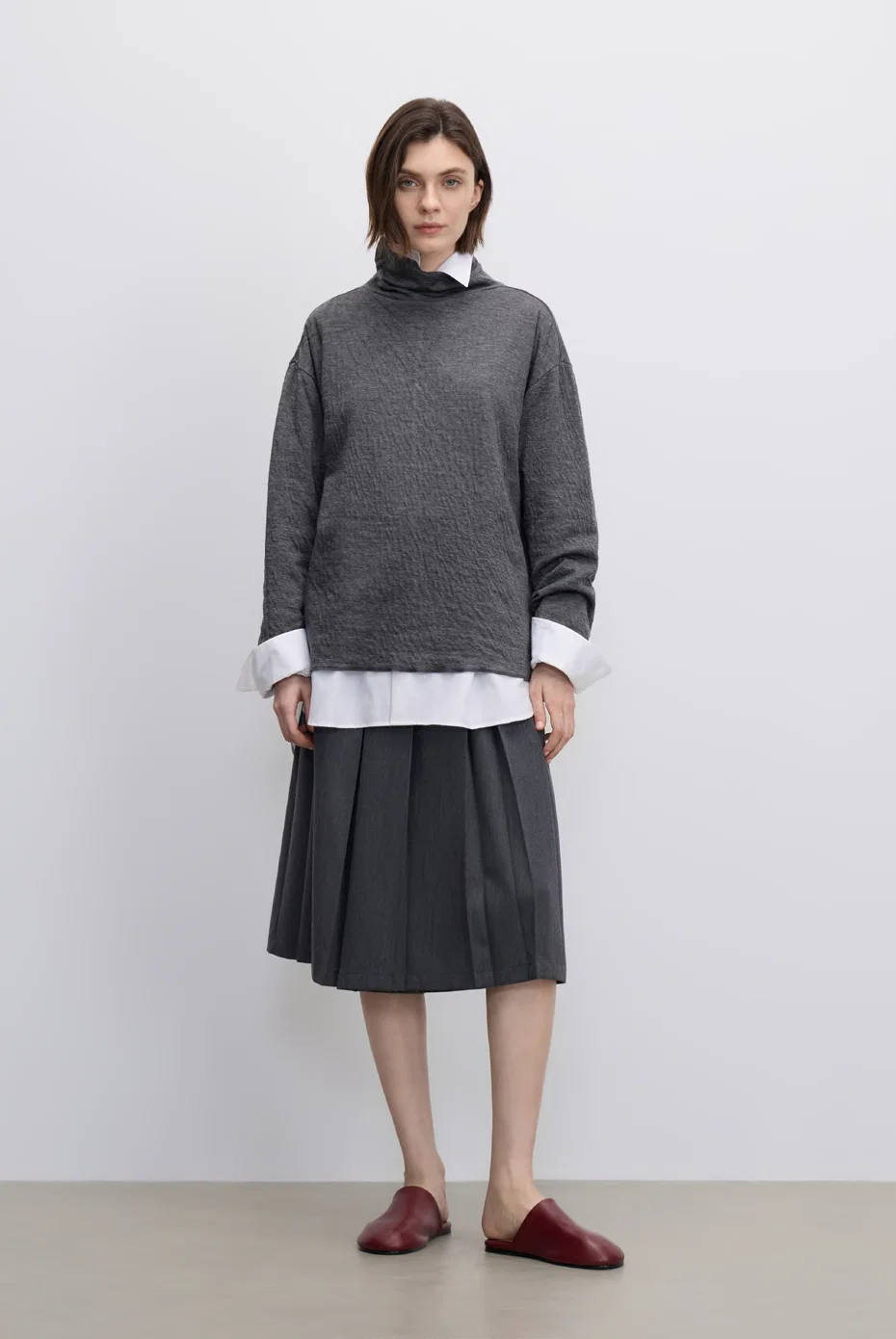 Grey sweater layered over a white shirt with a dark pleated skirt.