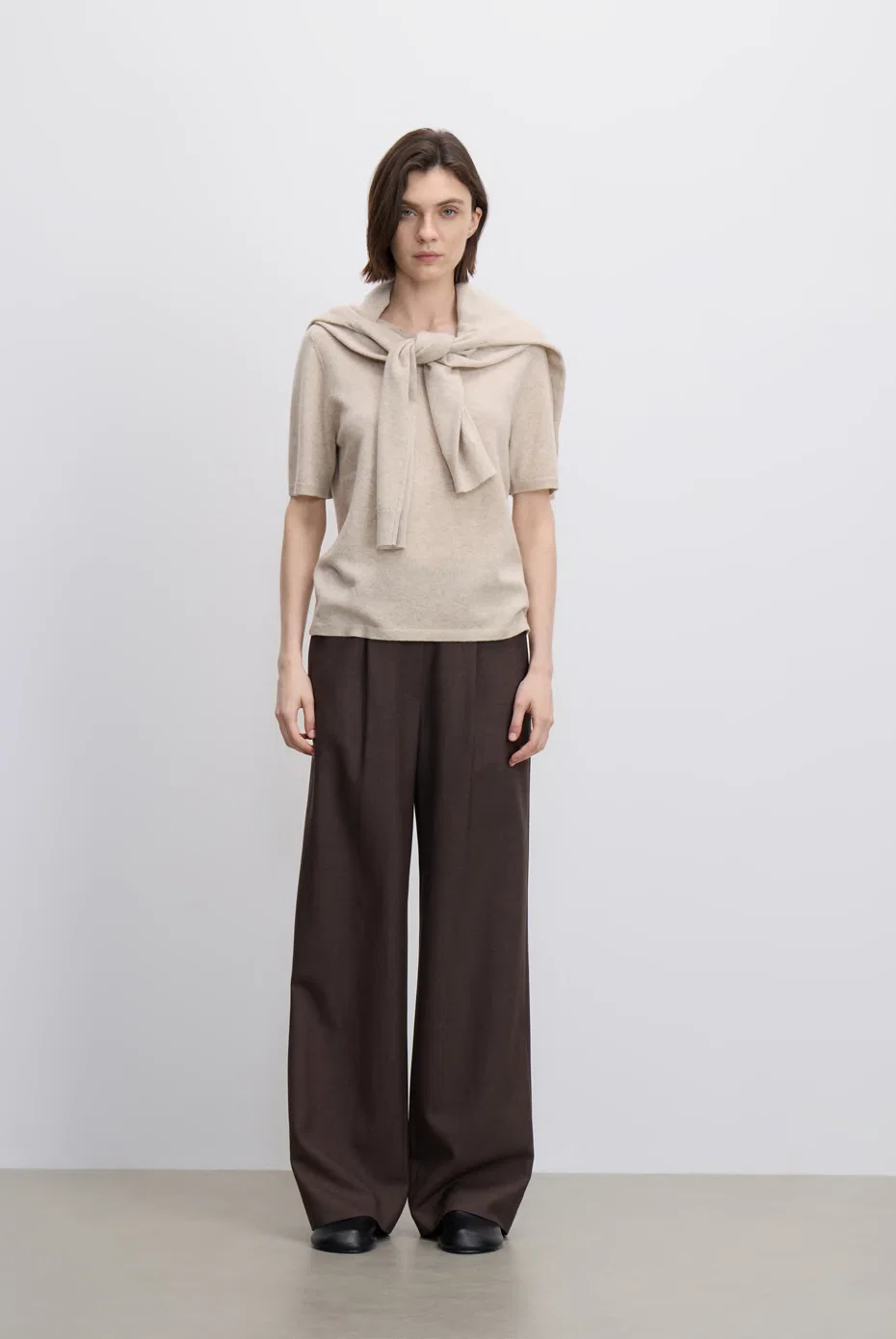 Beige scarf-detail top with brown wide-leg trousers.